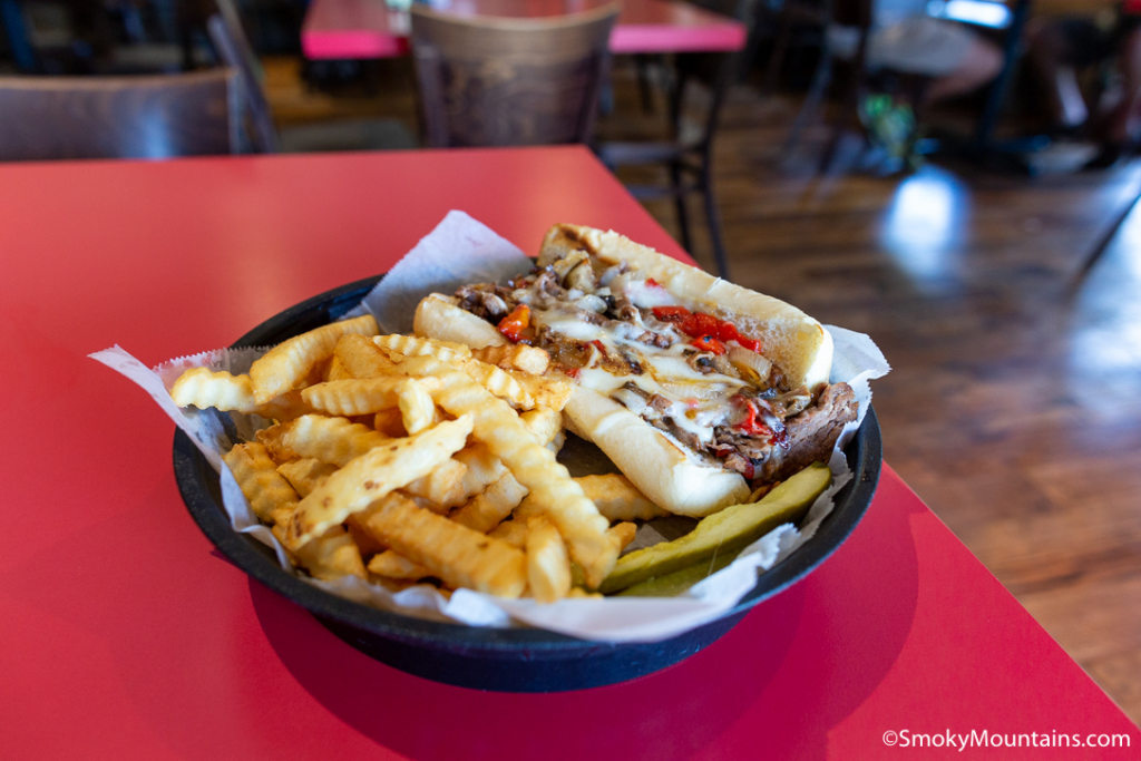 hot dog in bun next to a side of fries on red tabletop