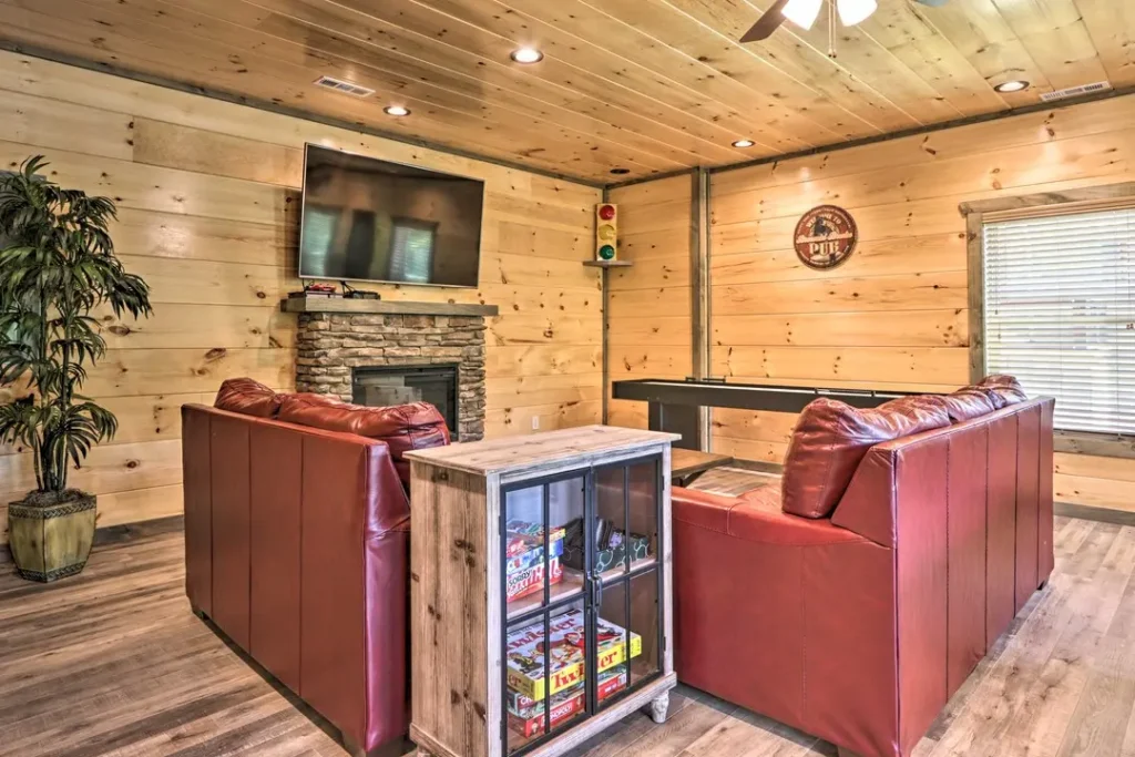 game room of cabin with stone fireplace, shuffleboard, large plant, and board game sin cabinet