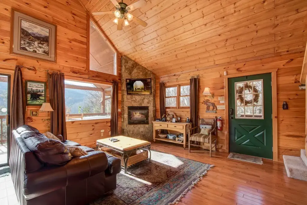 living room with brown leather couch, green door, and stone fireplace with tv